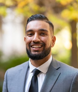 Smiling young man with short beard and business attire against natural backdrop