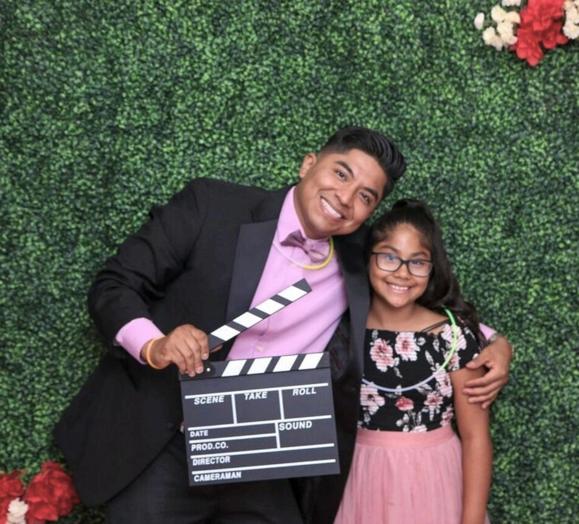 YoungSmiling Latinx father and daughter in formal attire against a natural backdrop