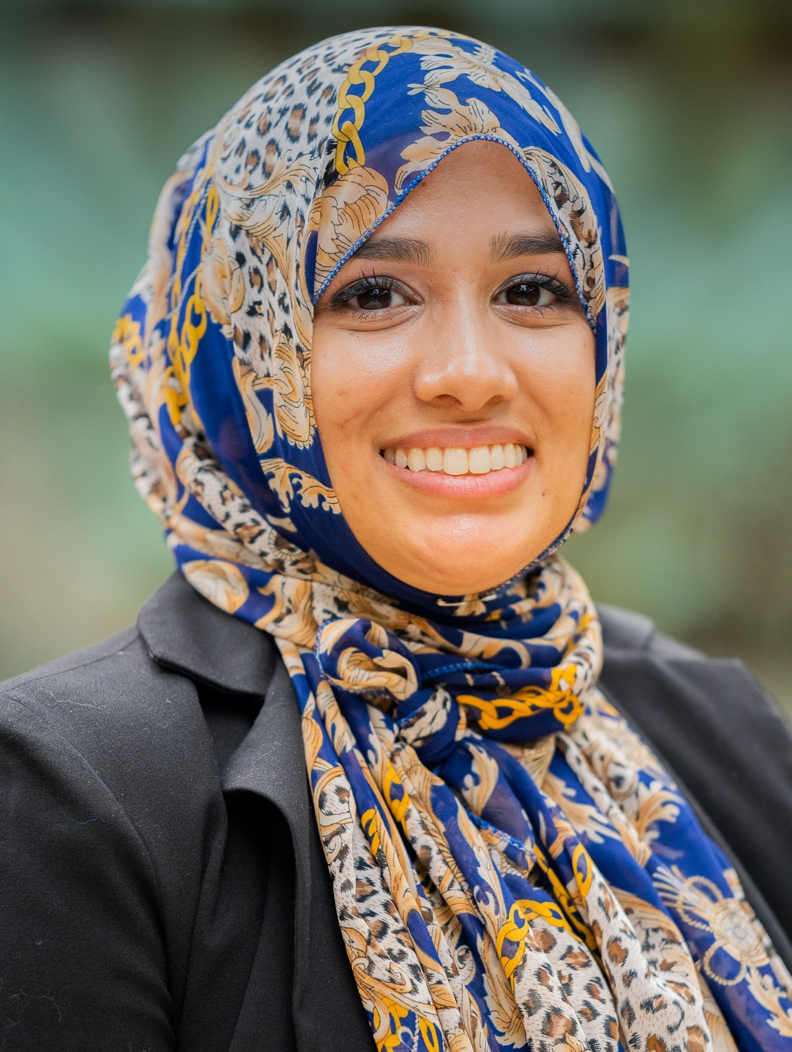 A smiling young woman in business attire and a colorful headscarf
