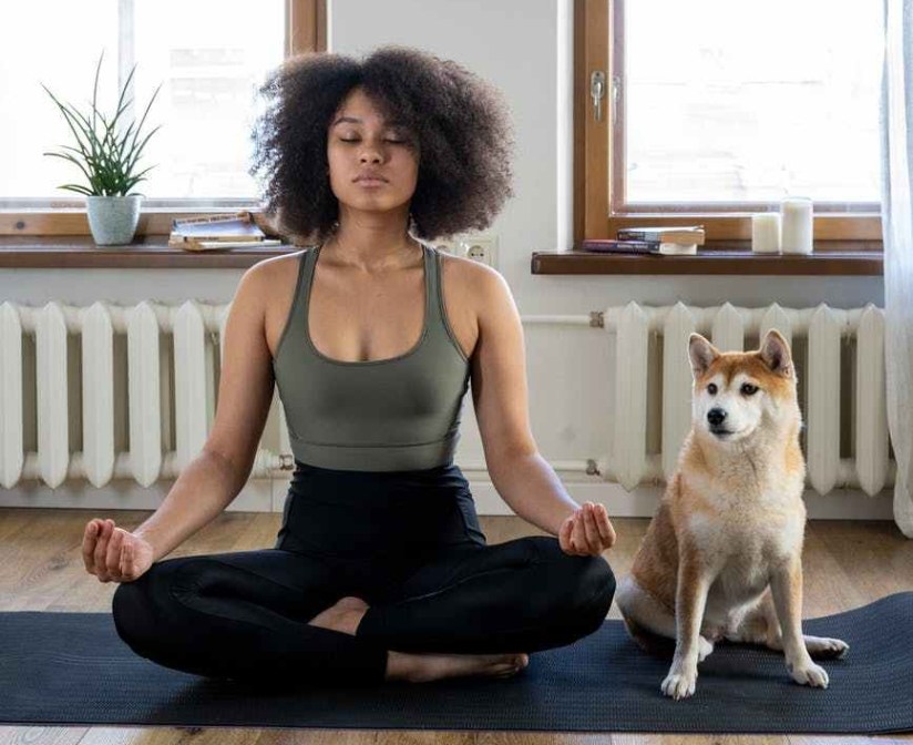 Athletic young woman of color sits in lotus position next to a dog in a peaceful room